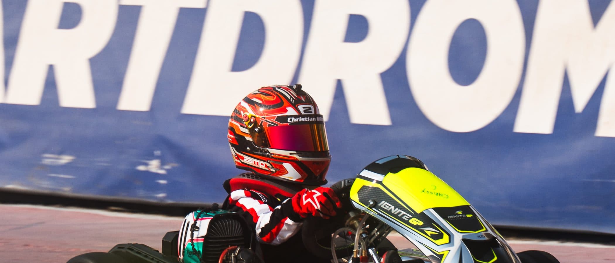 Bambino driver in profile in front of the Dubai Kartdrome banner