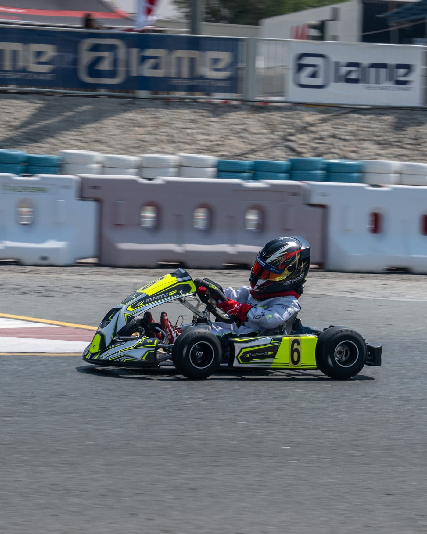 Bambino kart at speed past the white barriers, the grandstand banners behind