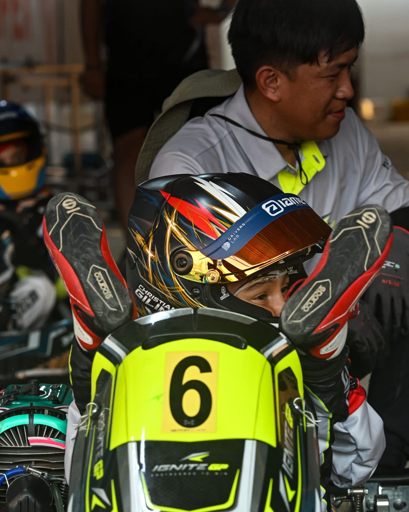 Bambino driver sitting in the kart under the awning before the session, a coach beside him